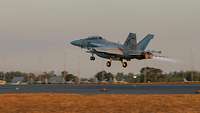A fighter jet takes off from an airfield at dusk.