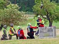 Flughelfer beim Lasteinhängen Fünf Personen knien auf einer Wiese. Neben ihnen steht ein Transportbehälter.
