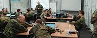 In einem Raum sitzen Soldatinnen und Soldaten unterschiedlicher Nationen zusammen