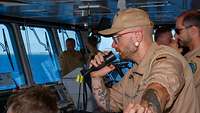 Ein Mann in brauner Marineuniform spricht in ein Handmikrofon