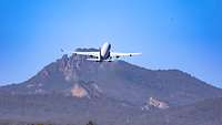 Ein Flugzeug vom Typ A330 MRTT startet vor einer bewaldeten Berglandschaft.