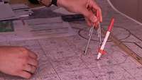Something is drawn on a map with a compass while pieces of paper lie in the background.