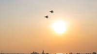  Two jets fly over anchored ships in front of the setting sun