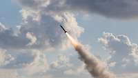 Symbolbild Tomahawk Von der unteren Seite des Bilds fliegt eine Rakete durch das Bild, im Hintergrund ist bewölkter Himmel.