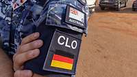 This picture shows the left shoulder of a blue-patterned uniform and a black-red-gold armband with the inscription “CLO”.