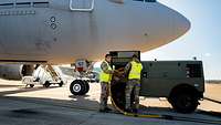 Two soldiers wearing high-visibility vests push a wiring harness in a green trailer in front of an aircraft