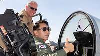 Ein koreanischer Pilot sitzt in einem geöffneten Cockpit während ein deutscher Pilot daneben steht. 