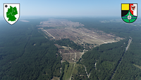 Luftaufnahme. Von Nadelwald umgebene Heidefläche. Fahrspuren von Fahrzeugen sind deutlich erkennbar.