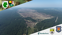Luftaufnahme. Von Nadelwald umgebene Heidefläche. Fahrspuren von Fahrzeugen sind deutlich erkennbar.