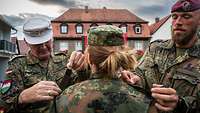 Zwei Soldaten legen einer Soldatin die zwei Schulterstücke an.