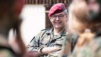 Ein General mit rotem Barett und Brille lächelt einer Soldatin zu, die vor ihm steht.