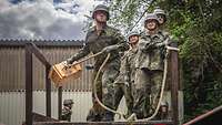 Von einem Podest aus schleudert ein Soldat eine Holzkiste an einem Seil, Soldaten stehen hinter ihm
