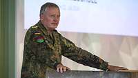 Ein General am Rednerpult während der Begrüßung, im Hintergrund eine Leinwand