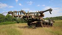 Ein Panzer mit einem Vorbau, an dem Ketten befestigt sind, steht auf einer Wiese.