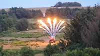 Ein Panzer steht auf Feld und stößt Feuerwerk nach oben aus. Es sind Rauchsäulen und Feuer zu sehen.