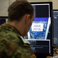 Ein Soldat sitzt vor mehreren Computerbildschirmen