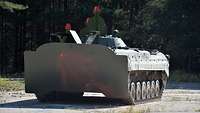 Ein Panzer steht auf einer Betonfläche neben Bäumen.