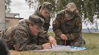 Drei Soldaten hocken auf einer Wiese und studieren eine Landkarte.