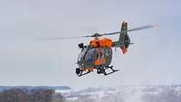 Ein Rettungshubschrauber vom Typ SAR H145M fliegt über eine Schneelandschaft