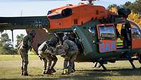 Soldaten vom Sanitätsdienst beladen einem Rettungshubschrauber mit einem Patienten