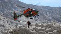 Ein Rettungshubschrauber vom Tap SAR H145M im Gebirge, während zwei Personen an einem Seil hängen