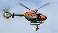 Ein Soldat wird mit einer Trage aus einem Rettungshubschrauber während des Fluges abgeseilt