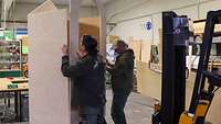 Zwei Männer fügen die einzelnen Bretter zu einem Wachhaus zusammen