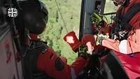 Zwei Soldaten sitzen mit Sicherheitsgurten in einem Hubschrauber während die Tür vor ihnen offen ist