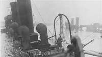 Schwarz-Weiß-Foto: Ein Mann an Deck eines fast vollständig gesunkenen Schiffes.