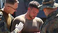 Ein Soldat mit einem blutigen Verband am Arm steht aufrecht. Er wird von einem weiteren Soldaten gestützt.