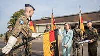 Eine Frau heftet ein Fahnenband an eine schwarz-rot-goldene Truppenfahne, die ein Soldat hält.