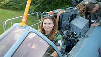 Ein Mädchen blickt aus einem Cockpit, dahinter ein Soldat, der sich vorbeugt und etwas zeigt. 