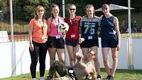 Gruppe von fünf Mädchen, davor liegt eine Soldatin, die einen Ball nach oben wirft.