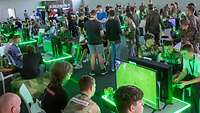 Blick über Computerbildschirme mit Fußballspiel in eine Halle voll junger Menschen an Spielkonsolen.