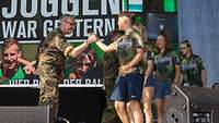 Ein Soldat macht einen Handschlag mit einer Sportlerin, die mit ihrem Team auf die Bühne kommt