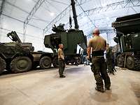 Mehrere Soldaten stehen in einer großen Halle. Ein Kran hebt ein Fahrzeugmodul an. 