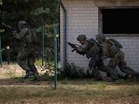 Zwei bewaffnete Soldaten gehen hinter einer weißen Häuserwand in Deckung, ein Soldat stürmt voran.