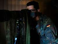 Ein Soldat sitzt im dunklen Raum und schaut durch eine getarnte Digitalkamera. 