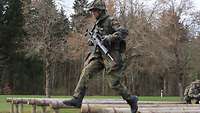 Ein Soldat mit Waffe läuft über ein Balkenhindernis.