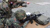 Ein Soldat liegt mit einer Waffe im Anschlag auf einer Matte, ein Ausbilder hockt neben ihm.