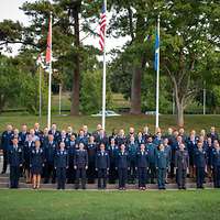 60 Reserveoffiziere in Dienstanzug posieren vor drei Flaggen, in der Mitte die der USA.