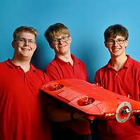 Drei Männer halten ein Gerät von einem Meter Länge mit Propellern im Gehäuse.