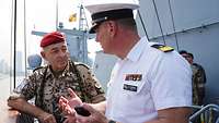 Ein Marinesoldat in weißer Uniform unterhält sich auf einem Schiff mit dem Generalinspekteur.