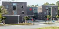 Ein moderner, dreigeschossiger Flachbau mit einem kleinen Roten Kreuz auf der verklinkerten Fassade