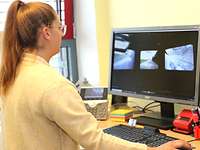 Eine Frau mit Brille und weißem Oberteil steht an einem Büroarbeitsplatz mit Computer