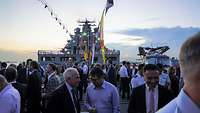Viele Menschen sind anlässlich eines Empfang auf einem Schiff bei Abendstimmung versammelt.