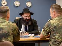 Rabbiner Oleg Portnoy im Gespräch mit Soldaten Ein Rabbiner mit schwarzem Hut unterhält sich an einem Tisch sitzend mit zwei Soldaten in Flecktarn