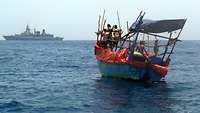 Ein Boot mit vier Personen fährt auf hoher See. Im Hintergrund ist ein Schiff zu sehen.