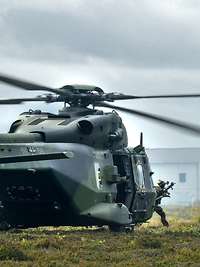 Aus einem Hubschrauber rennen mehrere Soldaten heraus, im Hintergrund Häuser.