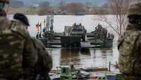 Soldaten überqueren mit einem Militärfahrzeug einen Fluss über eine militärische Behelfsbrücke